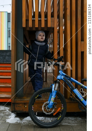 A European boy dressed in a winter jacket gets off his bike 113186334