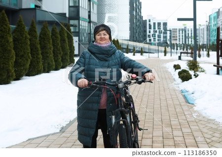Mature European woman spends active time and rides a bicycle in winter 113186350