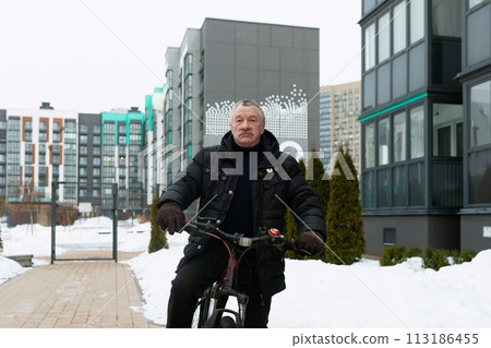 Mature man riding a bicycle in winter Mature man riding a bicycle in winter 113186455