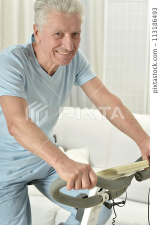 An elderly man is exercising on an exercise bike 113186493