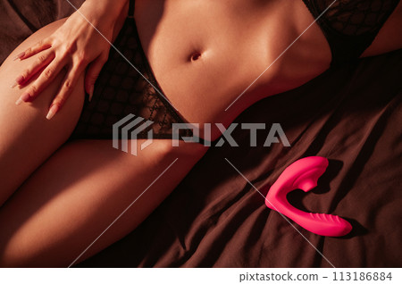 vibrator vacuum stimulator is lying nearby sexy female body. Girl woman in underwear is lying on a bed with sex toy at night in the bedroom 113186884