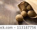 Potatoes in a jute bag on a wooden table 113187756