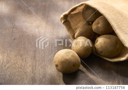 Potatoes in a jute bag on a wooden table Potatoes in a jute bag on a wooden table 113187756
