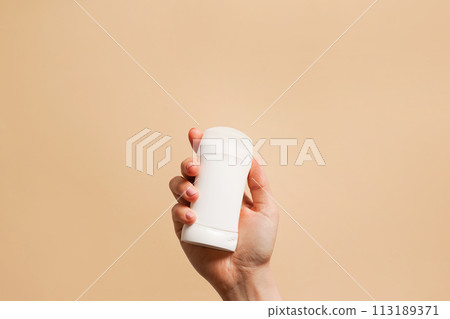 Hand holding antiperspirant, white deodorant on beige background, copy space 113189371