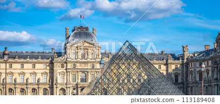 The Louvre Museums classical architecture contrasts with the modern glass pyramid under a blue sky with scattered clouds. The Louvre Museums classical architecture contrasts with the modern glass pyramid under a blue sky with scattered clouds. 113189408