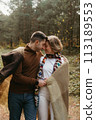 A man and a woman covered in a blanket snuggled up to each other in the middle of the forest, a couple enjoying time together outside the city 113189553