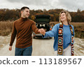 Smiling couple holding hands, strolling down country road with car on the background, happy man and woman on a roadtrip 113189567