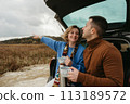 Happy young woman and man sitting in the open trunk of a car while traveling in autumn, road trip concept 113189572
