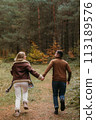 Adult couple having fun together in autumn park, a man and a woman are holding hands while running through the woods 113189576