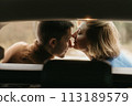 Intimate moment woman and man sitting in the open trunk of a car while traveling in autumn and kissing 113189579