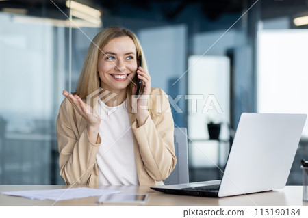 Cheerful businesswoman engaged in a pleasant conversation on her smartphone, smiling as she talks in a modern office. 113190184