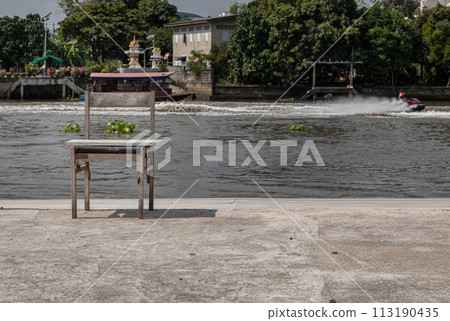 The old wooden chair is in front of the river, which is on the cement floor. The old wooden chair is in front of the river, which is on the cement floor. 113190435