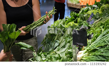 Young woman with little daughter buying fresh herbs at grocery. Choosing long beans, bunching onion and spinach Young woman with little daughter buying fresh herbs at grocery. Choosing long beans, bunching onion and spinach 113193242