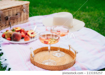 Pink drinks, cocktail with ice, raspberry, rosemary. Two glasses with martini, champagne, cider, lemonade on the blanket with fruit plate, picnic basket, Cozy summer picnic on nature. Selective focus. Pink drinks, cocktail with ice, raspberry, rosemary. Two glasses with martini, champagne, cider, lemonade on the blanket with fruit plate, picnic basket, Cozy summer picnic on nature. Selective focus. 113193257