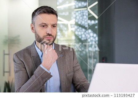 A focused businessman in a suit at his workplace, engaging in serious contemplation with a hand on his chin. A focused businessman in a suit at his workplace, engaging in serious contemplation with a hand on his chin. 113193427