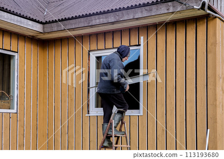 Exterior window finishing with metal jambs and mouldings, construction worker working standing on stepladder. Exterior window finishing with metal jambs and mouldings, construction worker working standing on stepladder. 113193680