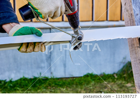 Electric drill shear sheet metal cutter, roofing iron cutting tool, worker removes excess part from galvanized steel sheet when finishing external openings of windows of rural house. 113193727