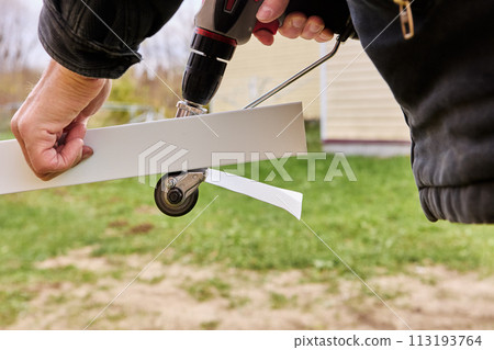 Sheet metal cutting gears are rotated by an electric drill, being adapter attachment, roofer cuts roofing steel outdoors. Sheet metal cutting gears are rotated by an electric drill, being adapter attachment, roofer cuts roofing steel outdoors. 113193764