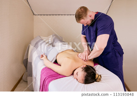 Massage therapist comes to home with massage table and gives back massage to young woman. 113193848