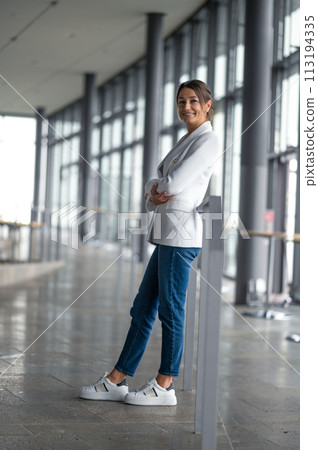 Confident elegant woman in white jacket standing in the premises with big windows 113194335