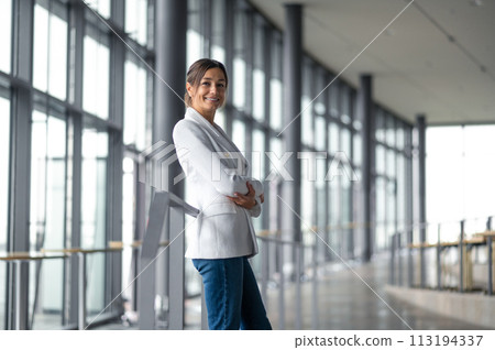 Confident elegant woman in white jacket standing in the premises with big windows 113194337