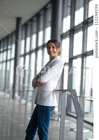 Confident elegant woman in white jacket standing in the premises with big windows 113194339