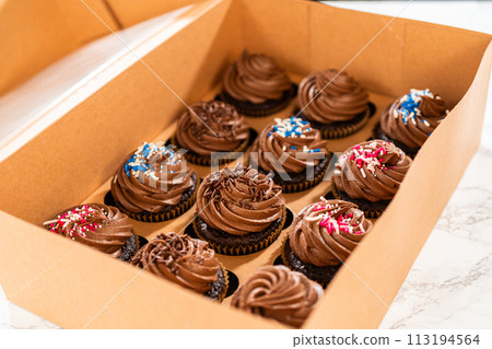 Preparing to share the delicious chocolate cupcakes, the final step involves carefully packaging them into a brown paper cupcake box. 113194564