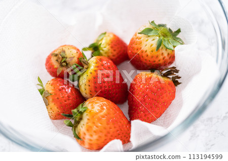 Freshly washed and dried strawberries are carefully arranged in a glass bowl lined with paper towel, ready for snacking or further use. 113194599