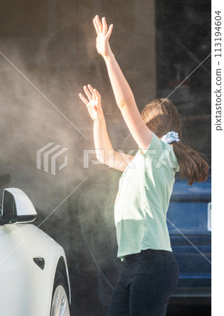 A young girl enthusiastically assists in washing the family's electric car in their suburban driveway. 113194604
