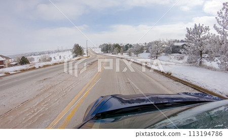 Traversing a freshly cleared, suburban road after a winter storm, one experiences a serene drive through an upscale residential neighborhood. Snow-covered houses and trees contribute to a picturesque 113194786