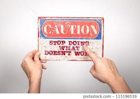 Stop Doing What Doesn't Work. Metal warning sign in a woman's hand on a white background Stop Doing What Doesn't Work. Metal warning sign in a woman's hand on a white background 113196539