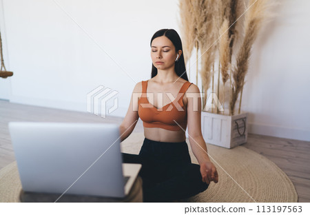 Calm woman in earbuds meditating in lotus pose Calm woman in earbuds meditating in lotus pose 113197563