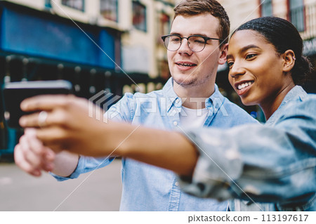 Positive dark skinned hipster girl with caucasian friend making photo on phone for blog Positive dark skinned hipster girl with caucasian friend making photo on phone for blog 113197617