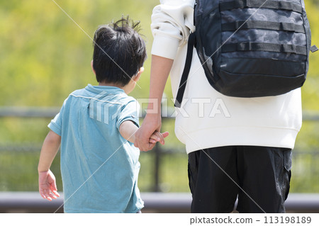 黃金週（黃金週）期間，一個孩子手牽手與父親在公園裡的新鮮綠色植物中玩耍，無臉的後視 113198189