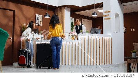Asian tourists entering hotel lobby and using service bell, ringing to call employees and offer support at check in. Travelers requesting assistance from front desk staff, hospitality industry. Asian tourists entering hotel lobby and using service bell, ringing to call employees and offer support at check in. Travelers requesting assistance from front desk staff, hospitality industry. 113198194