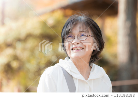 一位微笑的高級女性在背光秋葉中享受觀光、旅行等的輪廓 一位微笑的高級女性在背光秋葉中享受觀光、旅行等的輪廓 113198198