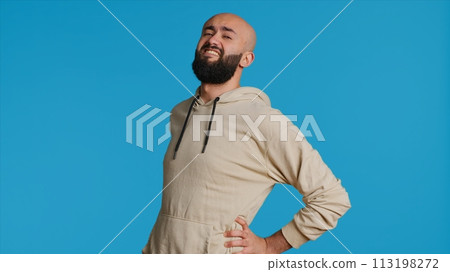 Middle eastern model dealing with lower back pain, having sore muscles because of bad posture. Arab person massaging the spine in pain to relieve discomfort in studio. Camera 1. Middle eastern model dealing with lower back pain, having sore muscles because of bad posture. Arab person massaging the spine in pain to relieve discomfort in studio. Camera 1. 113198272