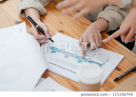 Close-up view of team members' hands pointing at a business growth chart during a strategic meeting. 113198749