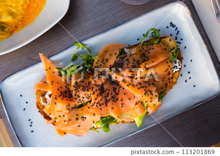 Delicious smoked salmon with arugula avocado and seeds on fried bread 113201869