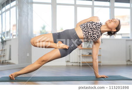 Sporty skilled young female teacher demonstrating side plank pose of yoga in training room Sporty skilled young female teacher demonstrating side plank pose of yoga in training room 113201898