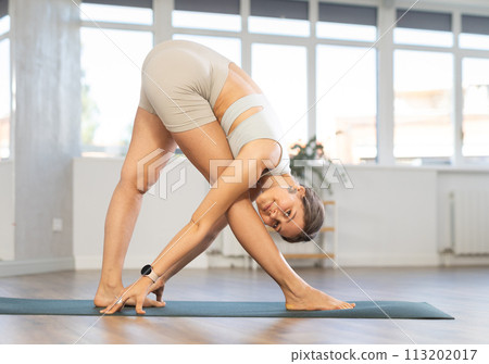 Sporty energetic female doing exercises parshvottanasana pose of yoga on pilates mat during training at gym 113202017