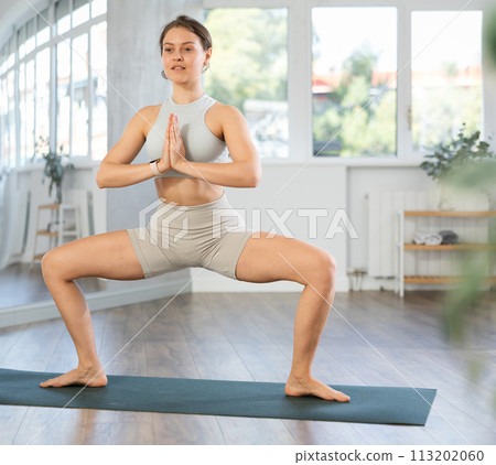 Girl performing Utkata Konasana with hands clasped in namaste 113202060
