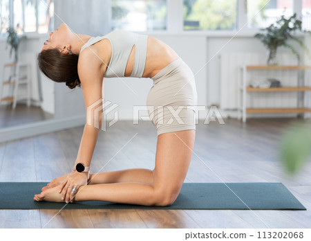 Skilled young female teacher demonstrating variation of camel pose of yoga in training room Skilled young female teacher demonstrating variation of camel pose of yoga in training room 113202068