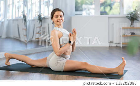 Experienced woman yoga trainer performing split pose pose on mat Experienced woman yoga trainer performing split pose pose on mat 113202083