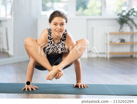 Smiling sporty girl performing shoulder-pressing pose Bhujapidasana 113202204