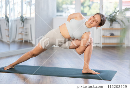 Slim girl practicing warrior pose of yoga on mat in fitness room 113202329