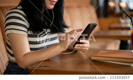 A woman sitting in a coffee shop, using her phone and listening to music on her headphones. 113203057