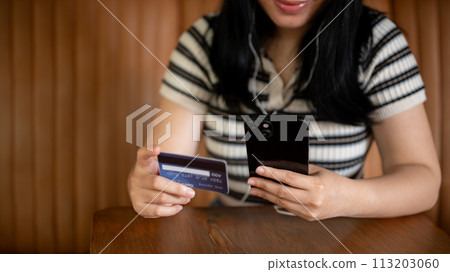 A cropped image of an Asian woman holding a smartphone and a credit card at a table in a coffee shop A cropped image of an Asian woman holding a smartphone and a credit card at a table in a coffee shop 113203060