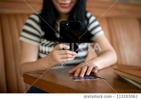 A woman registering her credit card on a shopping app on her mobile phone, sitting in a cafe. A woman registering her credit card on a shopping app on her mobile phone, sitting in a cafe. 113203062