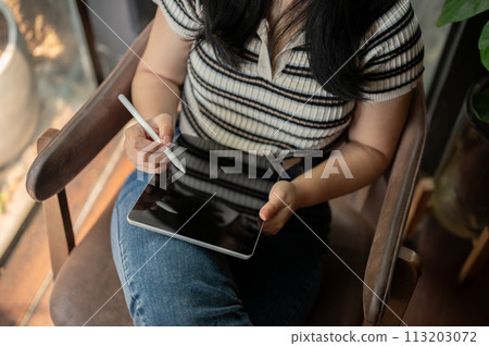 A cropped shot of an Asian woman using her digital tablet in a vintage green coffee shop. 113203072